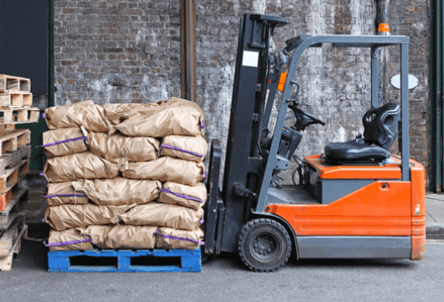 forklift holding stacks of brown bags on blue crate